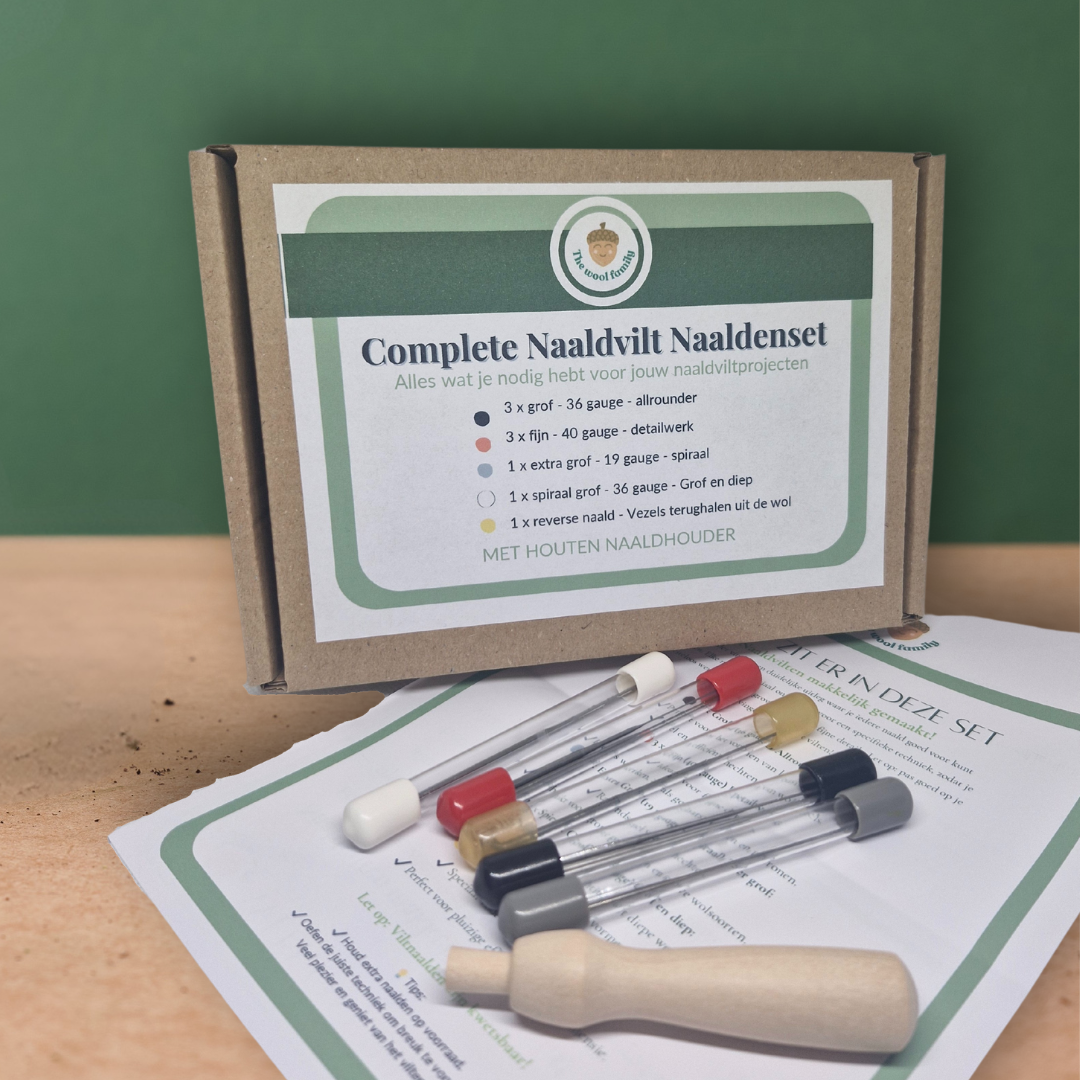 A set of needle felting needles with a wooden holder, displayed next to a box with the text 'Complete naad-vrij' (Always needle-free) and a reverse needle, on a table with a green background.